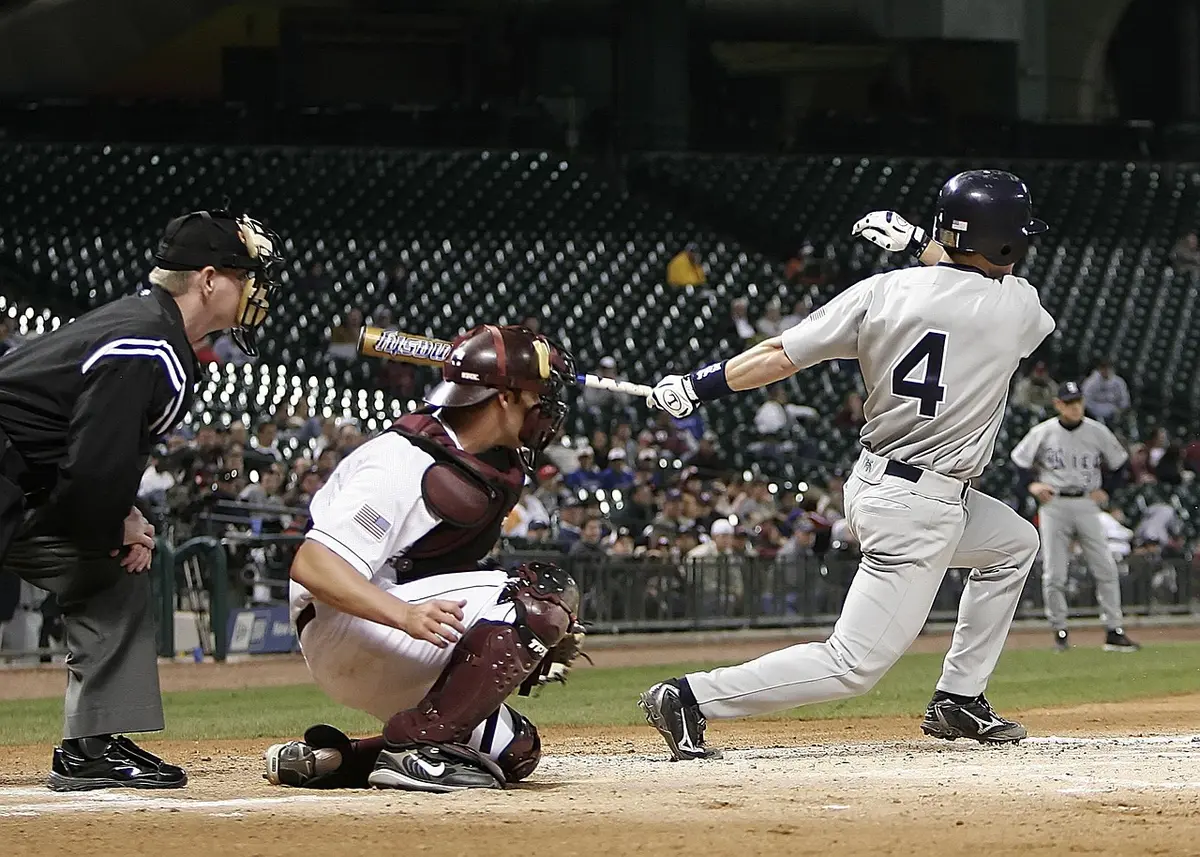 Two crossed baseball bats leaning against an outfield fence with a distant crowd