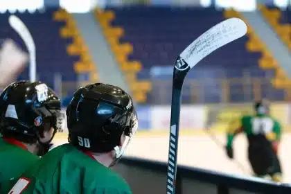 Anonymous player hands holding helmet on a hockey bench, team gear blurred behind