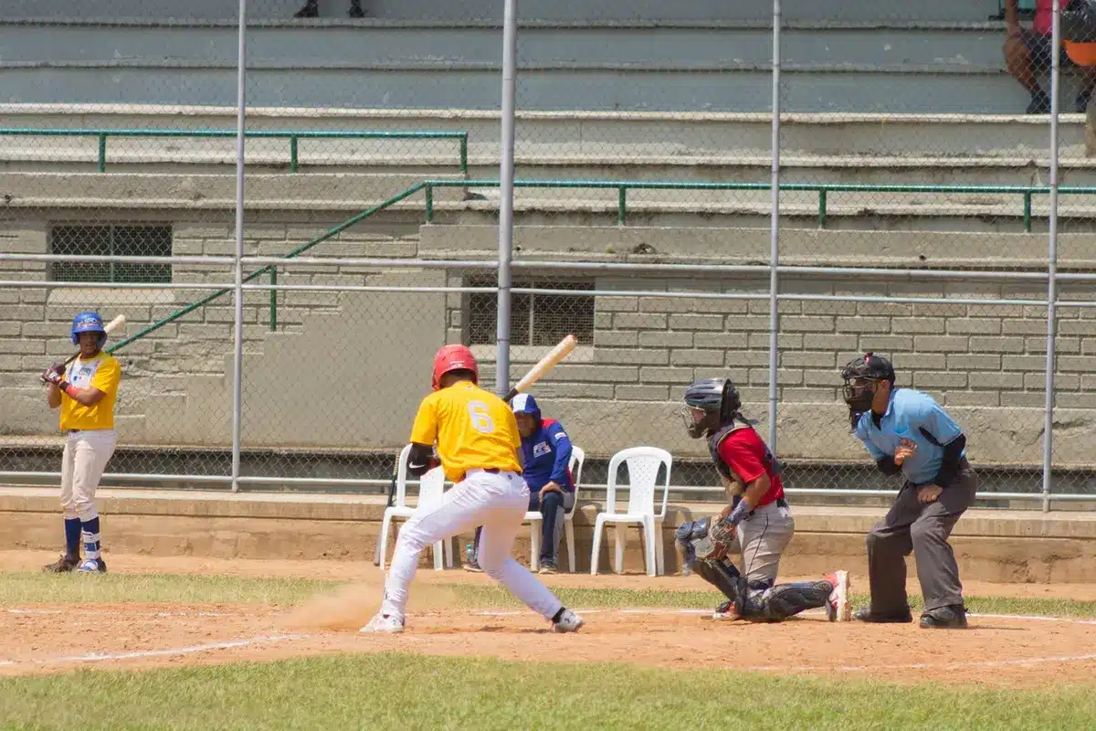 Late-inning dugout with bats and scorebook, bullpen mound visible in the distance