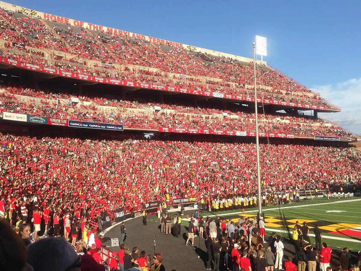Full stadium crowd cheering under lights during a big college game