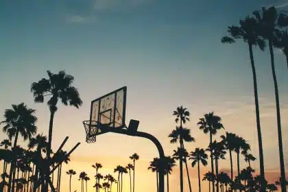 Silhouetted young basketball players and a coach practicing on an indoor court at dusk