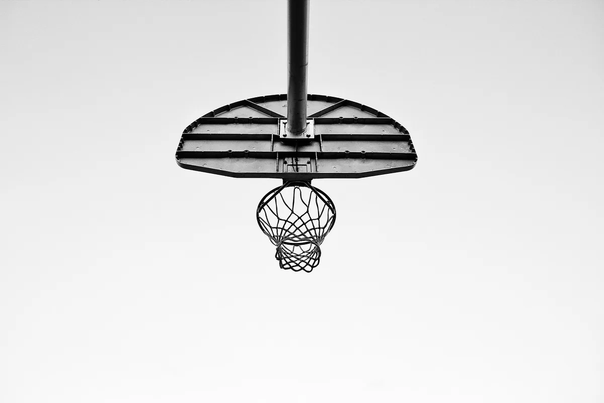 Silhouette of a basketball on a gym floor near bench and hoop during practice