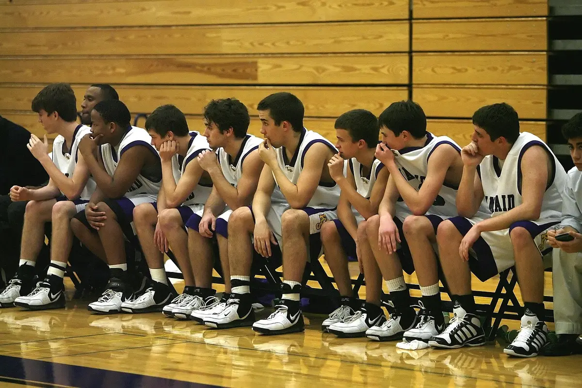 Coach talking with multiple wing players near the bench during practice